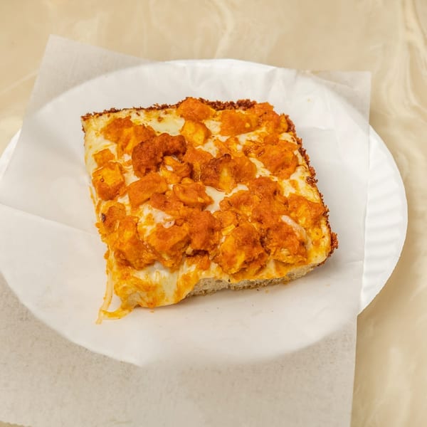 A square slice of Tori T's Pizzeria buffalo chicken pizza with melted cheese on a white paper plate.