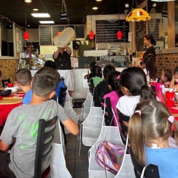 Kids in aprons watch a chef toss pizza dough at Tori T's Pizzeria.
