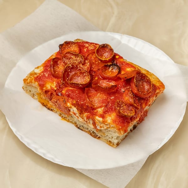 A thick slice of Tori T's pepperoni pizza with a rich red sauce on a white paper plate.