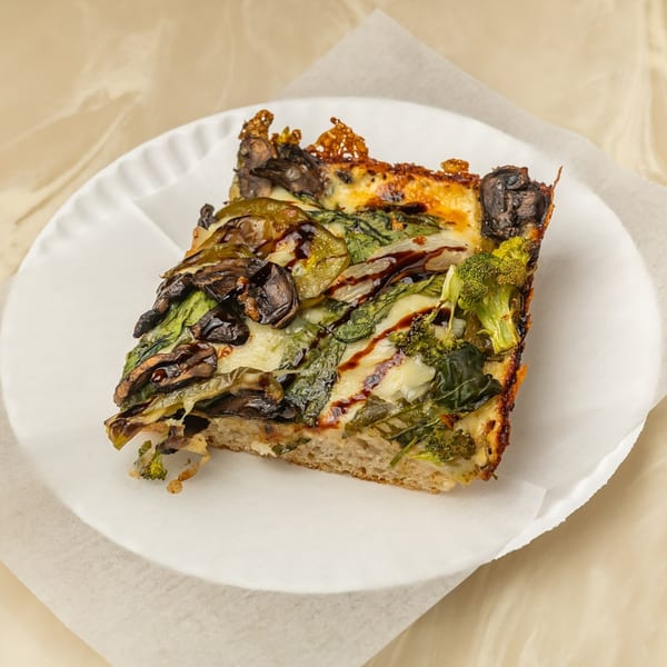 A square slice of Tori T's Pizzeria's vegetable pizza with broccoli, mushrooms, and spinach.