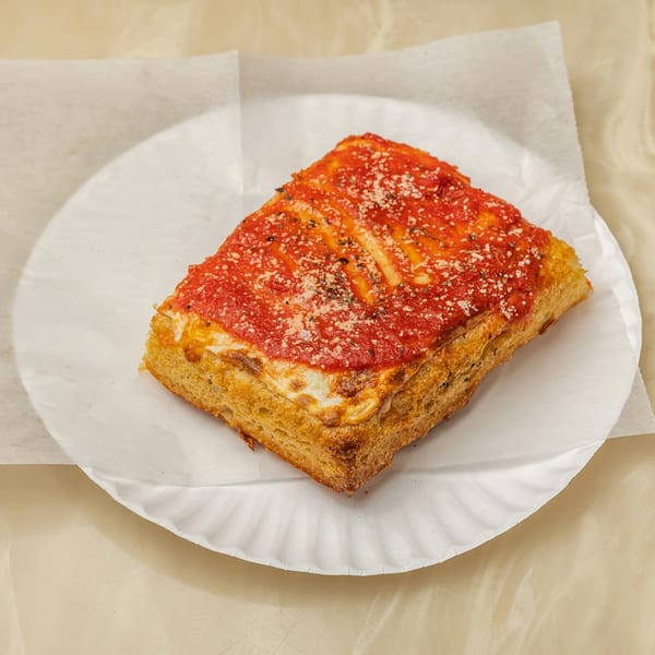 A thick, rectangular slice of Tori T's Pizzeria's Sicilian pizza with red sauce and cheese.